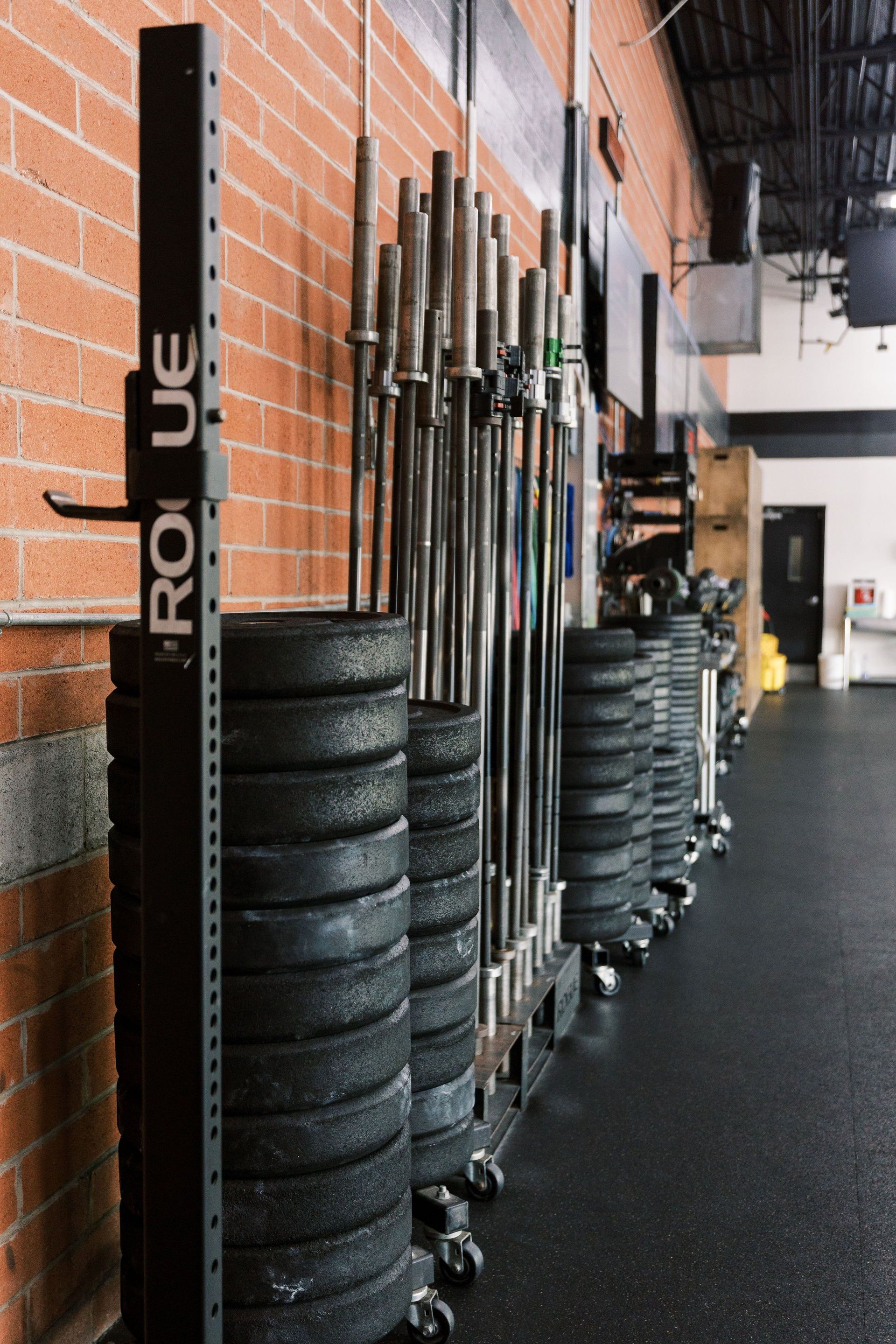 Row of stacked black weight plates and barbells in a gym beside a brick wall
