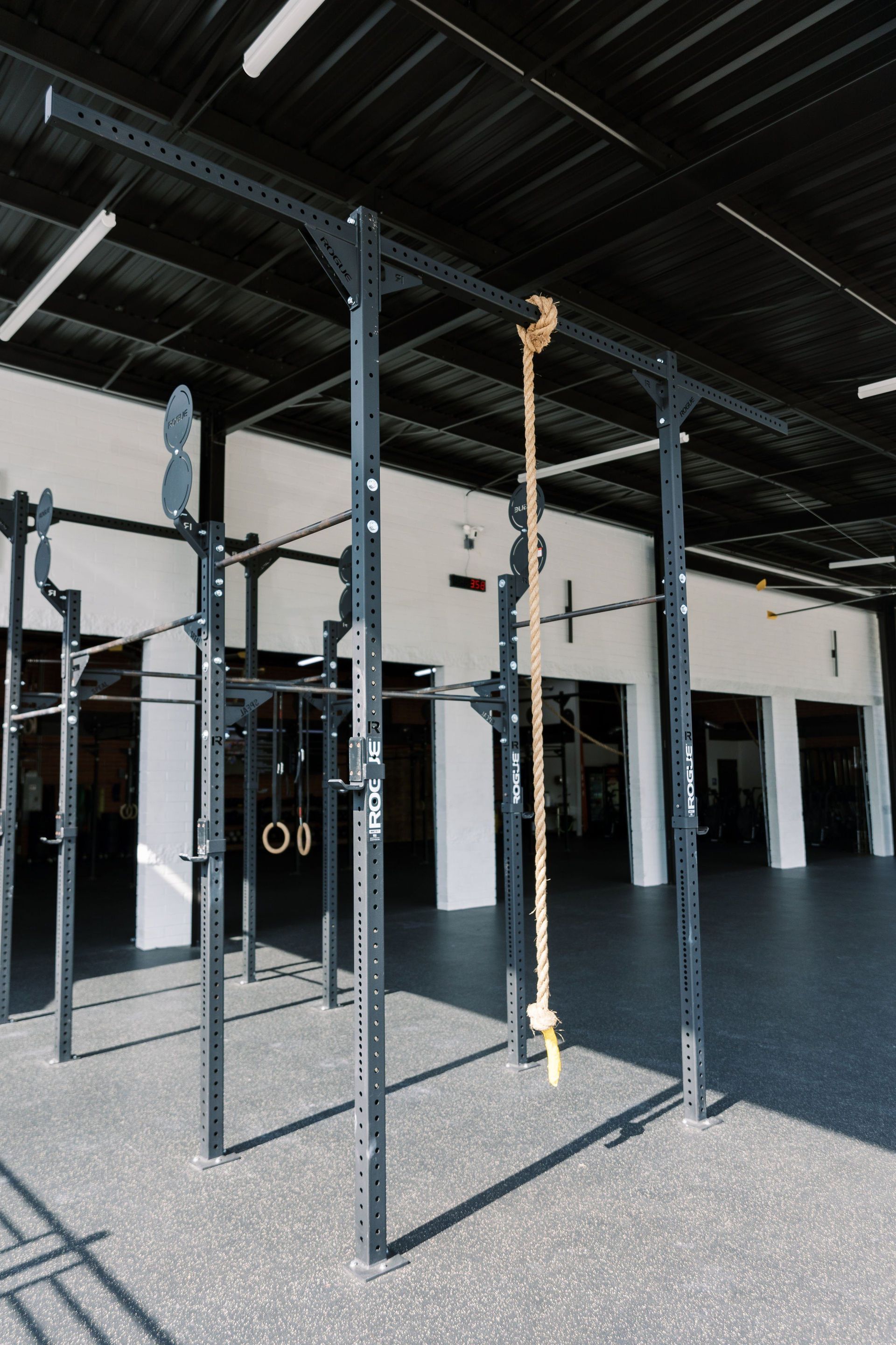 Indoor gym with black metal pull-up rigs and hanging rings under a high dark ceiling