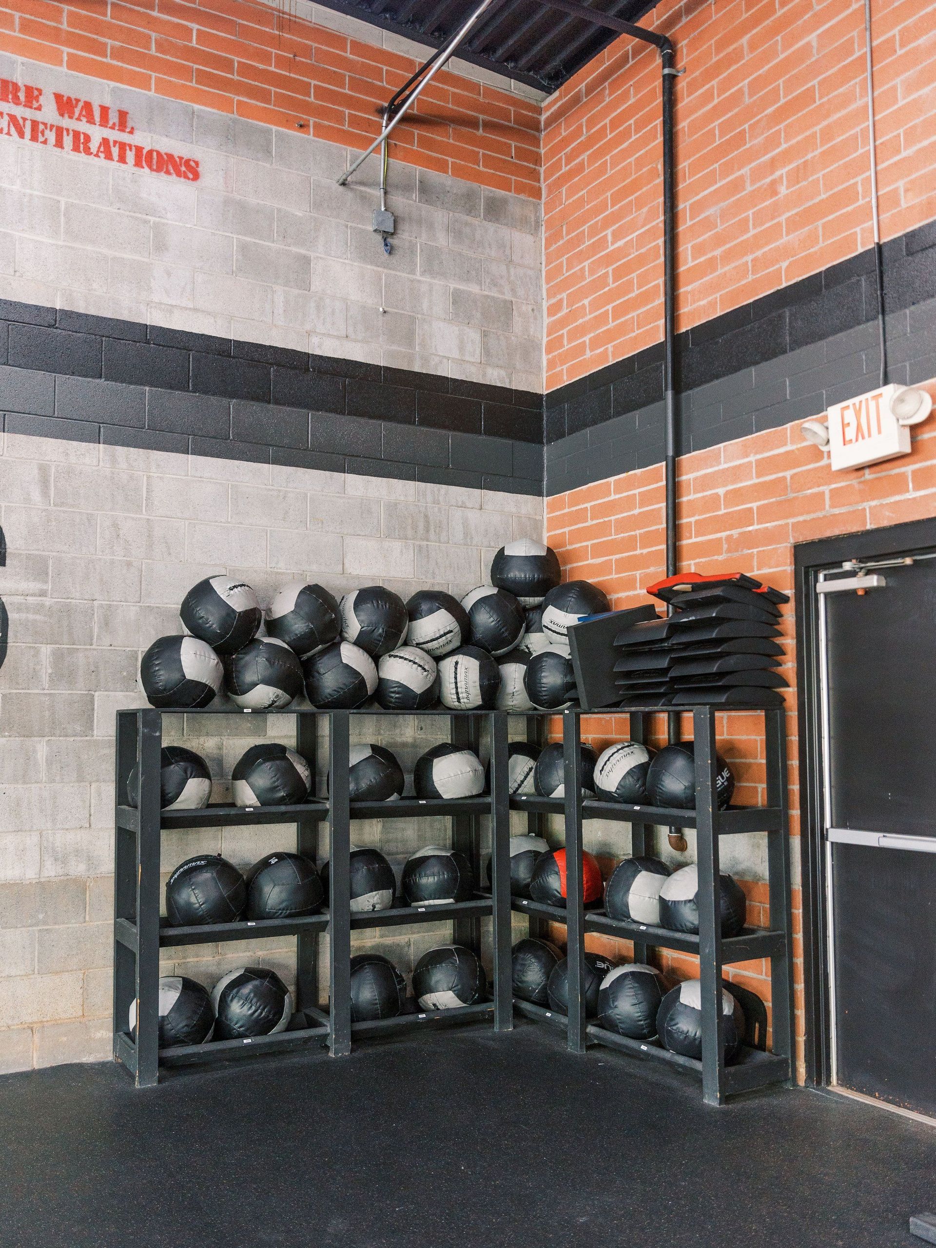 Gym storage corner with racks of medicine balls and exercise equipment against brick and cinderblock walls