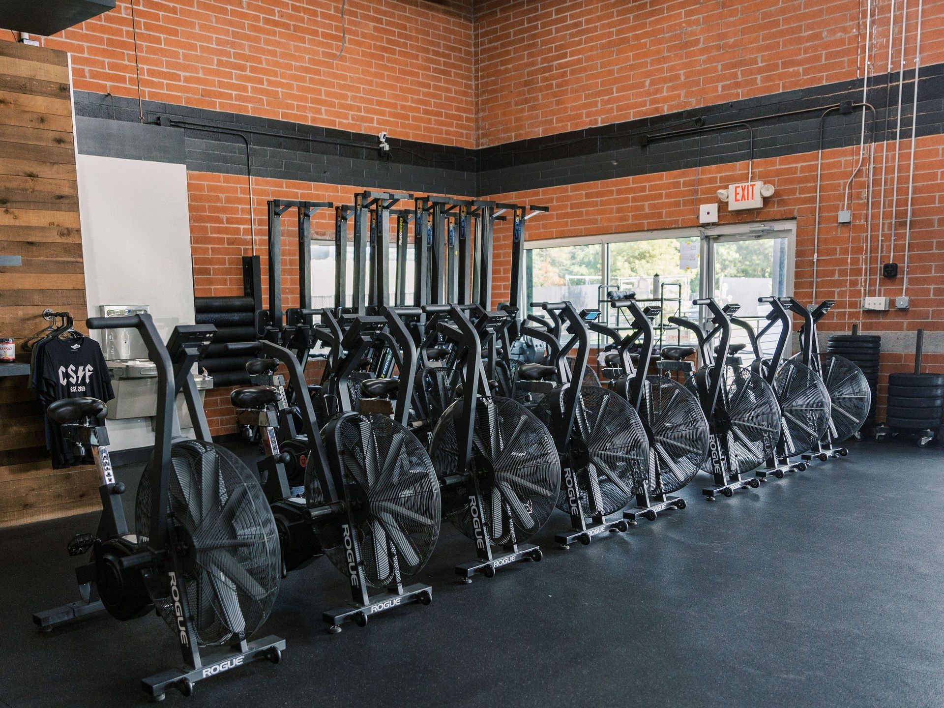Indoor gym with rows of black stationary bikes on a rubber floor and brick walls