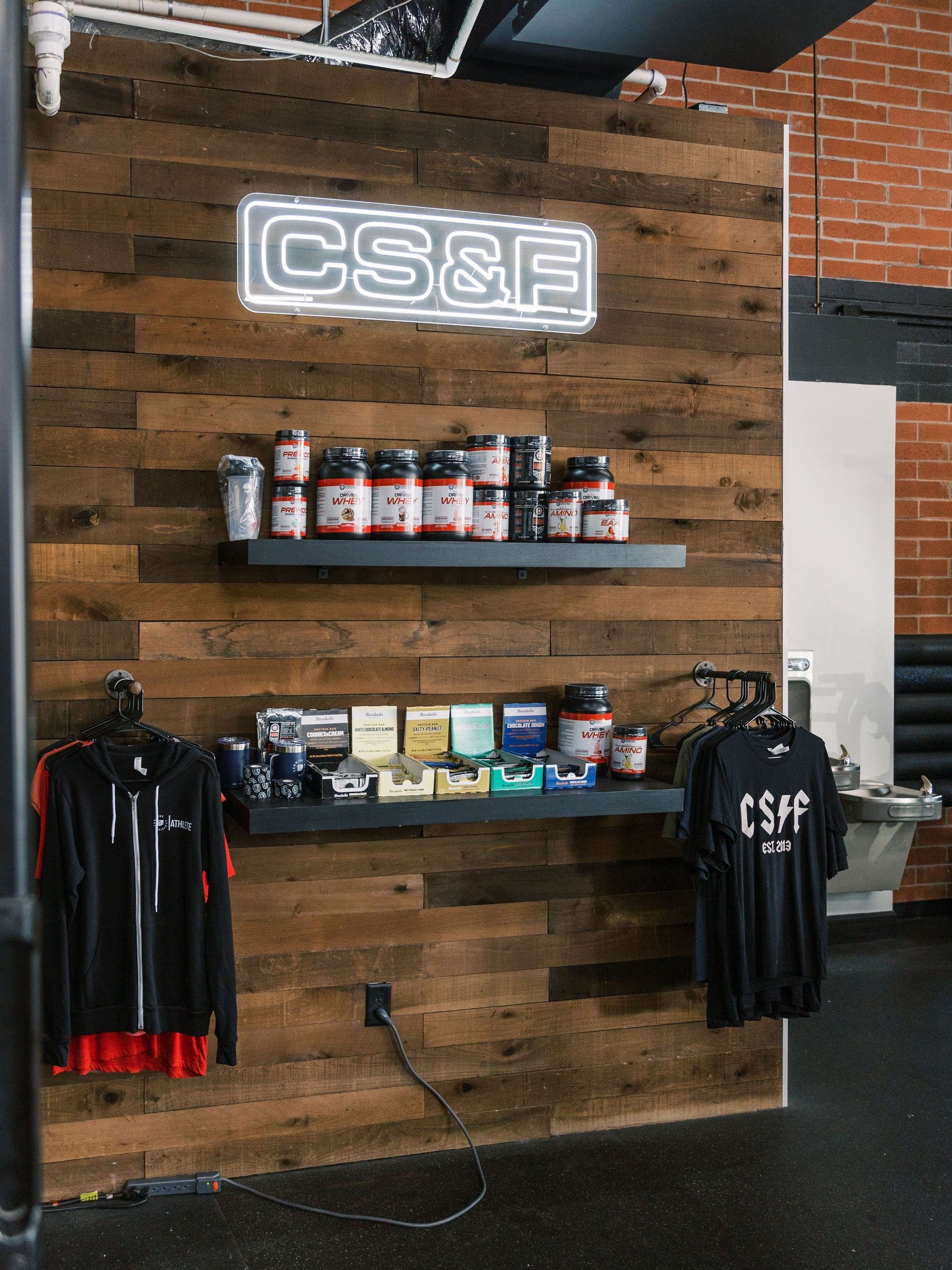 Neon CS&F sign above shelves of supplements and apparel on a rustic wood wall in a shop interior