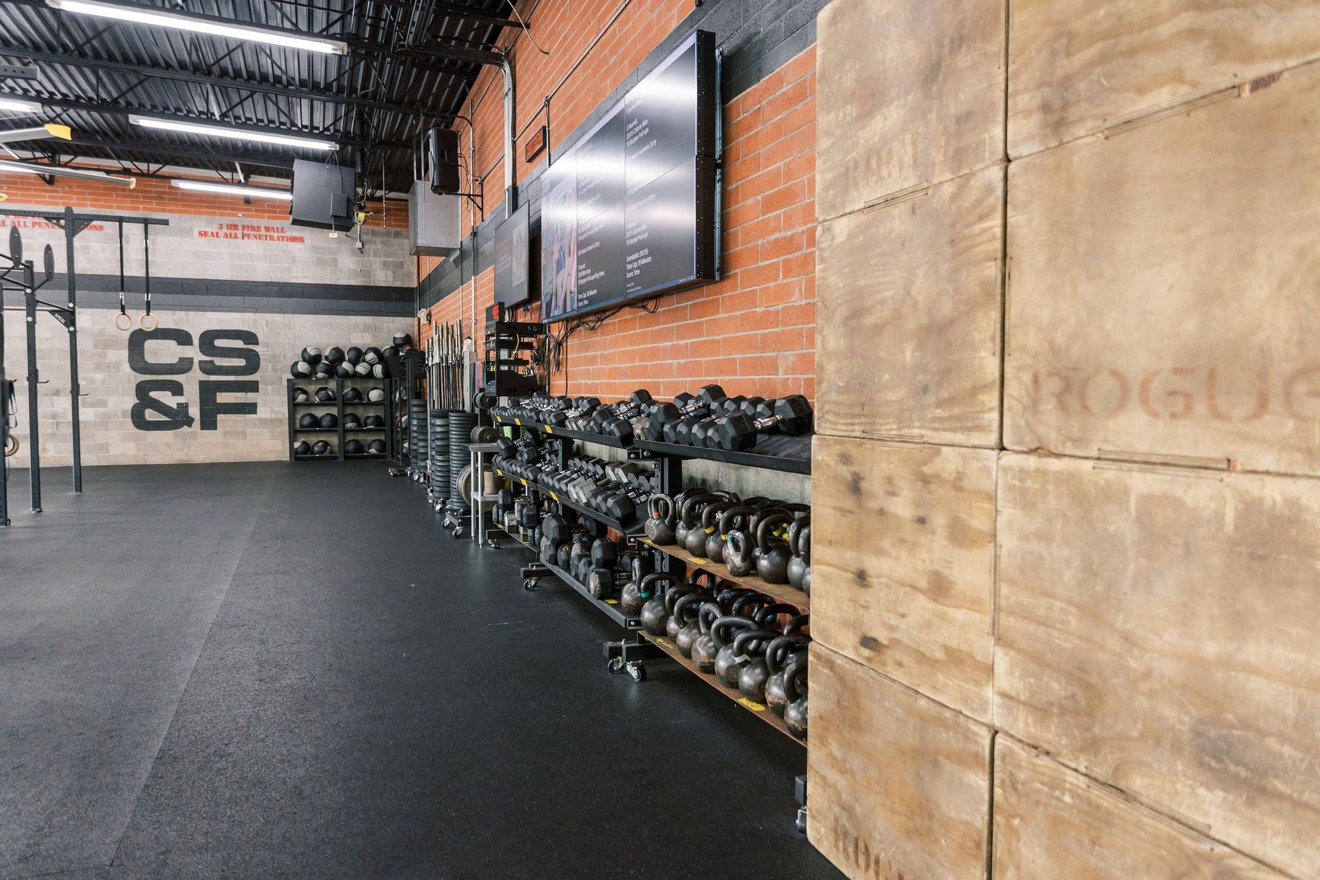 Indoor gym with brick wall, large screen, and rows of dumbbells along the wall