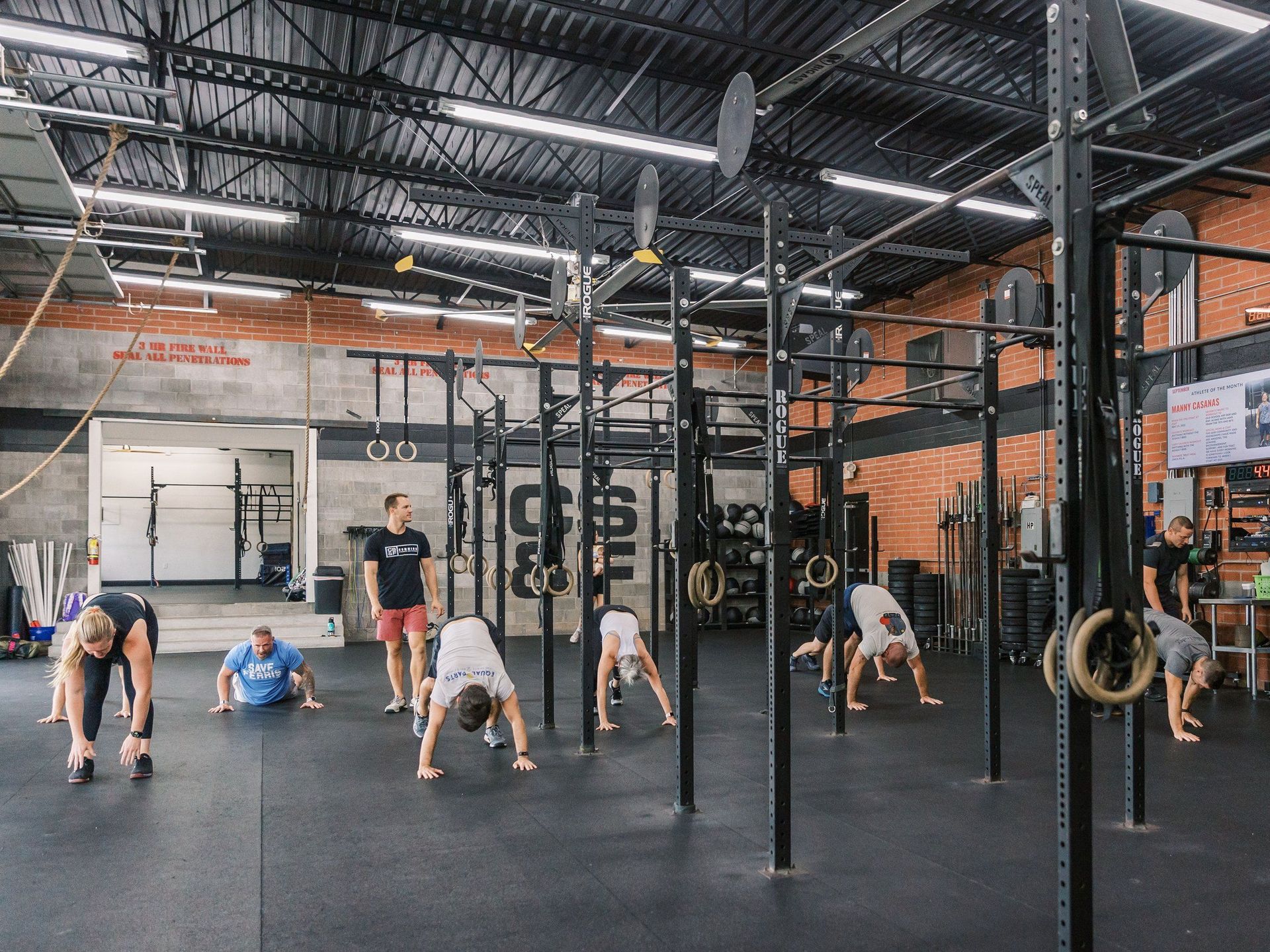 People exercising on mats in a CrossFit gym with pull-up rigs and hanging rings