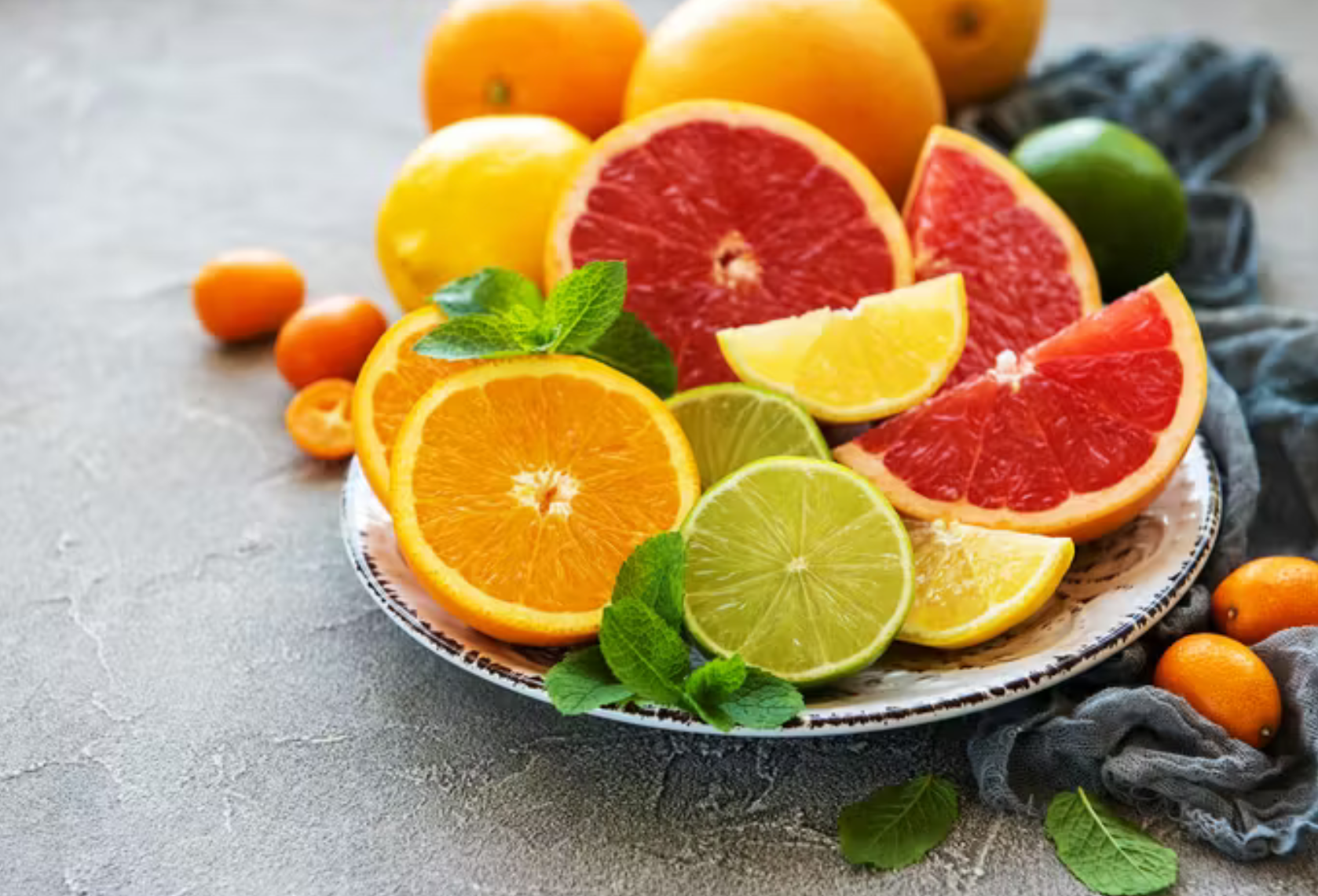 Plate of citrus fruits: oranges, grapefruit, lemons, limes, and kumquats, arranged with mint leaves.