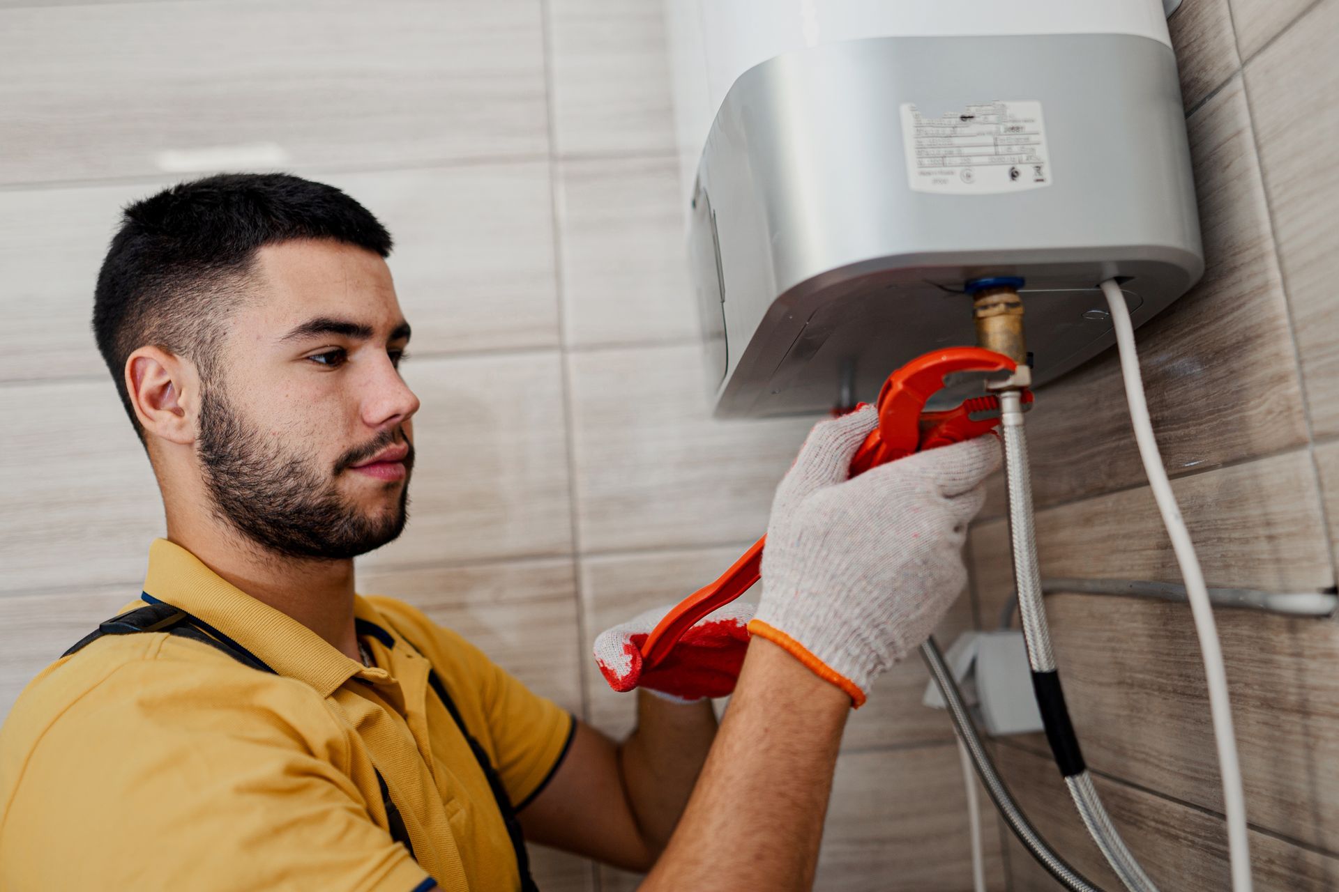 A man works on a water heater installation in a bathroom, using tools to complete the job.