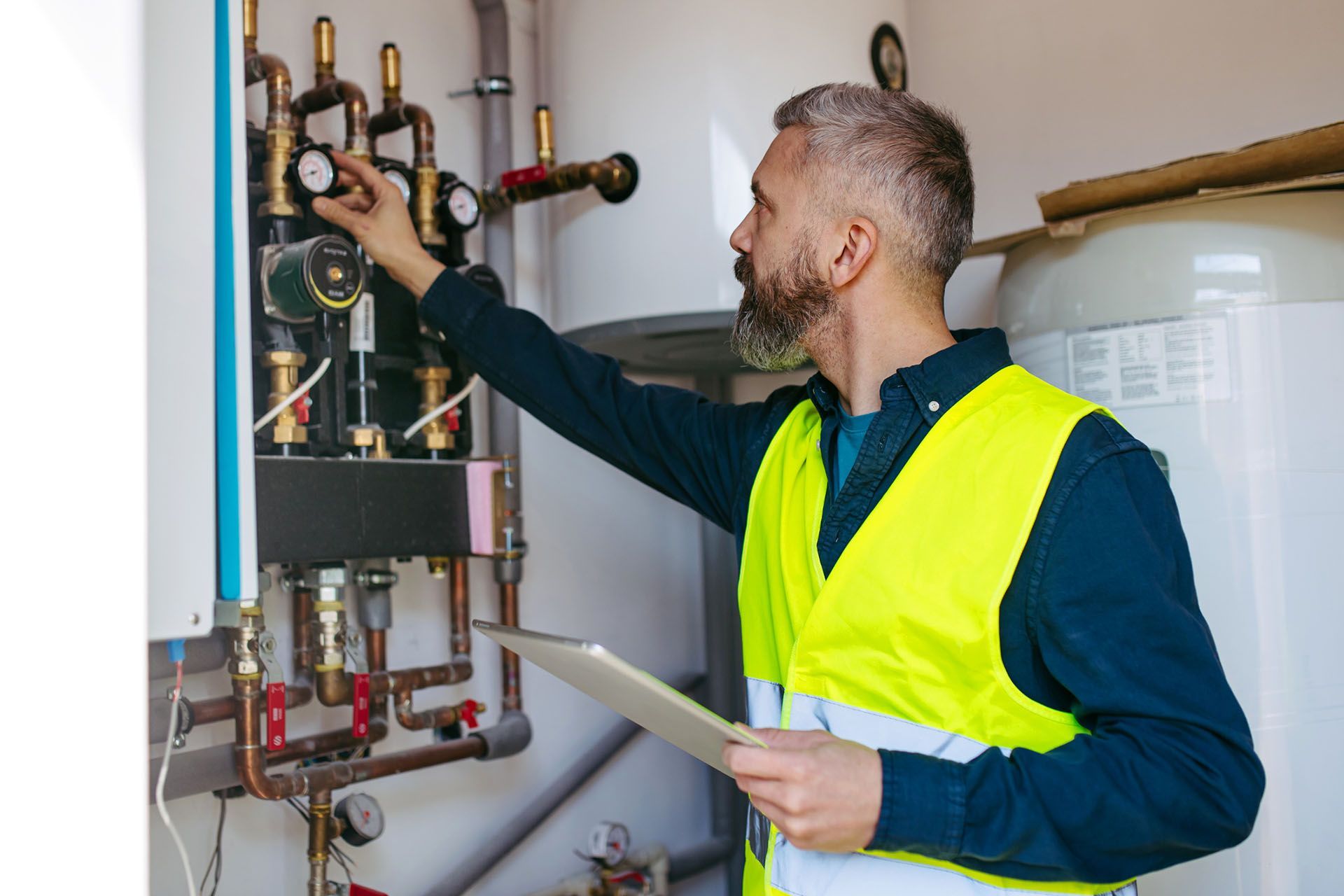 Technician checking boiler gauges while holding a clipboard in utility room.