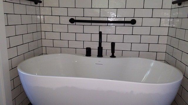 A white bathtub is sitting in a bathroom next to a white brick wall.