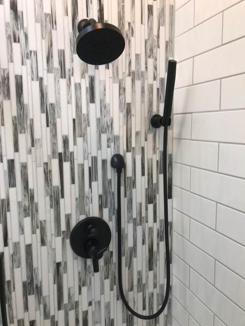 A shower with black shower heads and a white tile wall