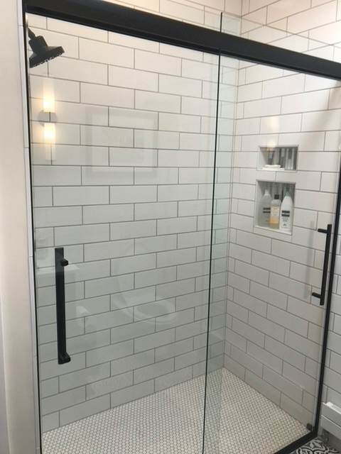 A bathroom with white tiles and a sliding glass shower door.