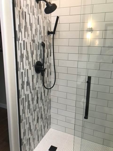 A shower with white tiles and a black shower head.