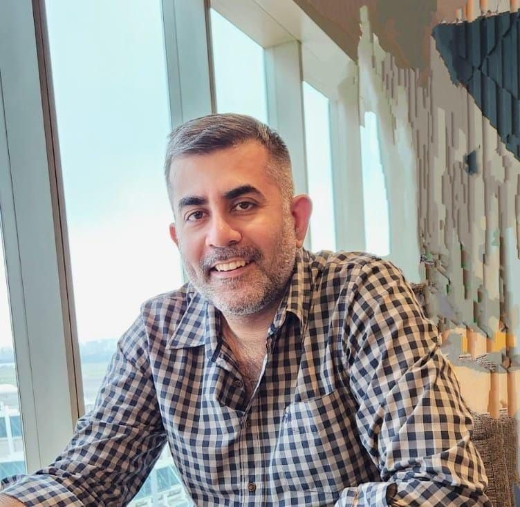 A man in a plaid shirt is sitting at a table in front of a window.