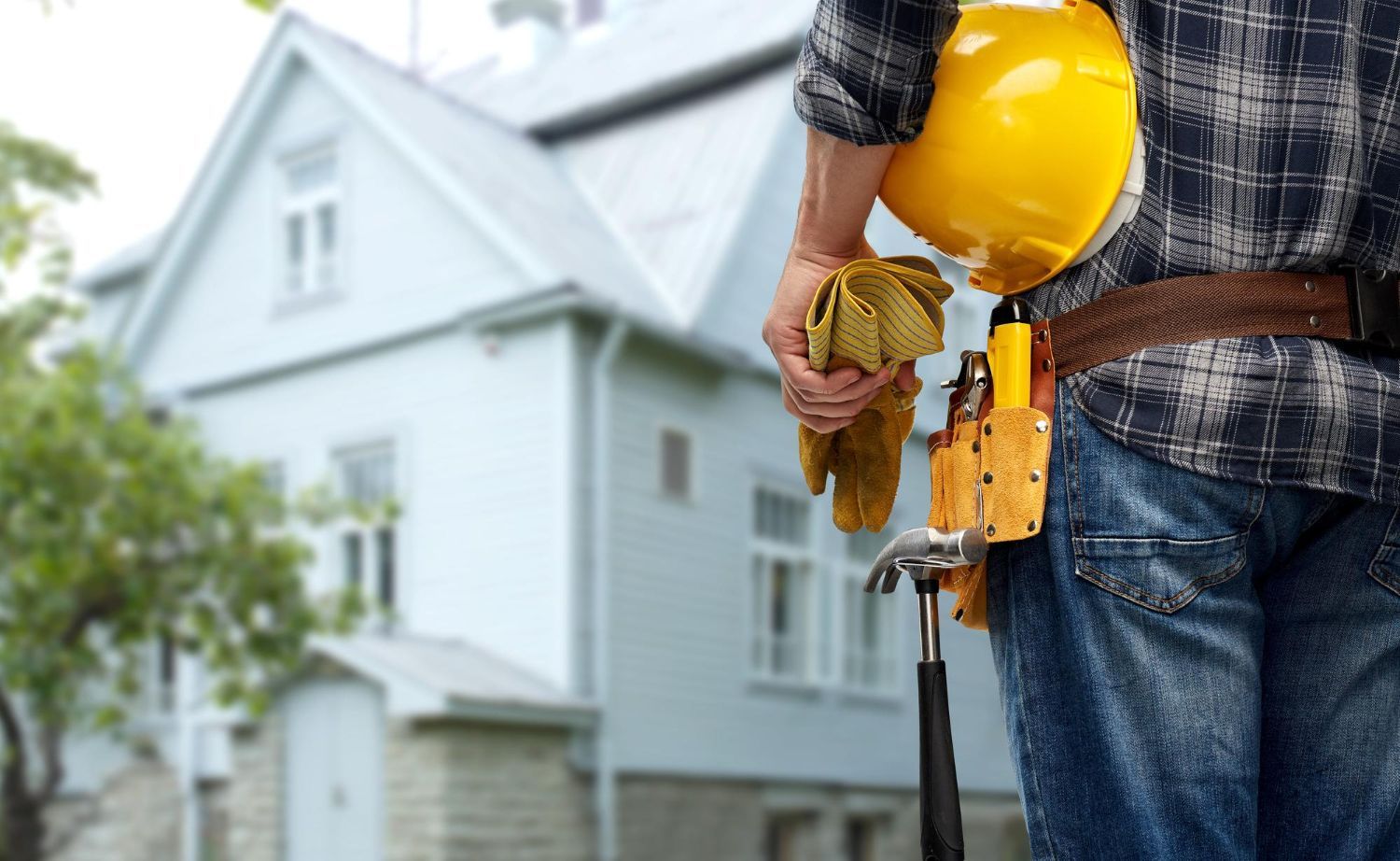 Construction worker holding a yellow hard hat and drill in front of a house