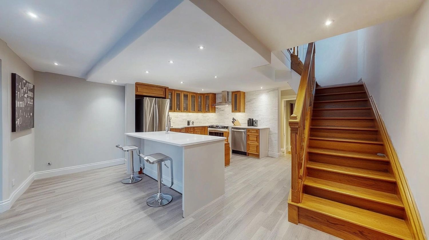 Bright open kitchen and dining area with white island, wood cabinets, and wooden staircase