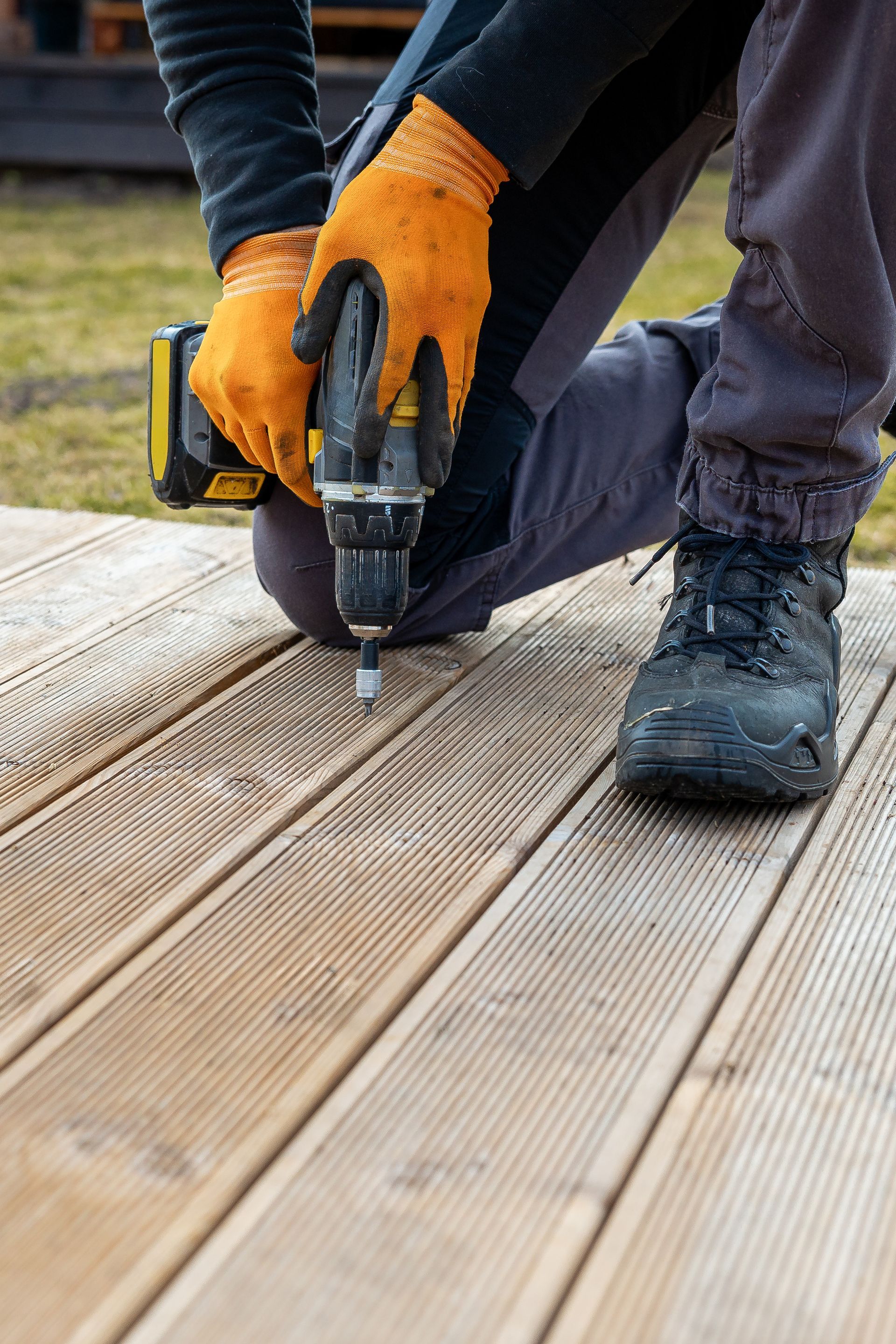 A person is using a drill on a wooden deck.