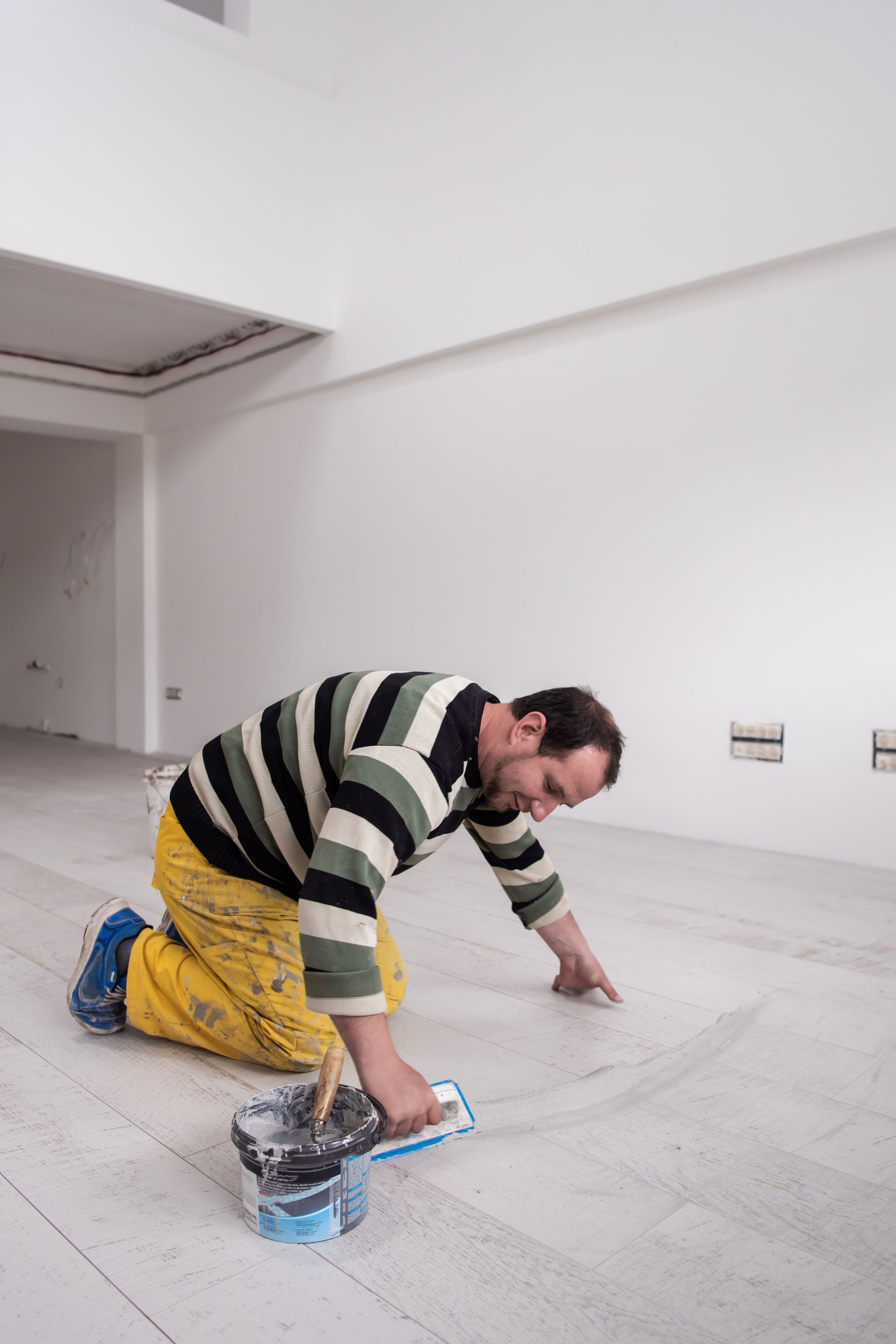 A man is kneeling on the floor with a bucket of paint.