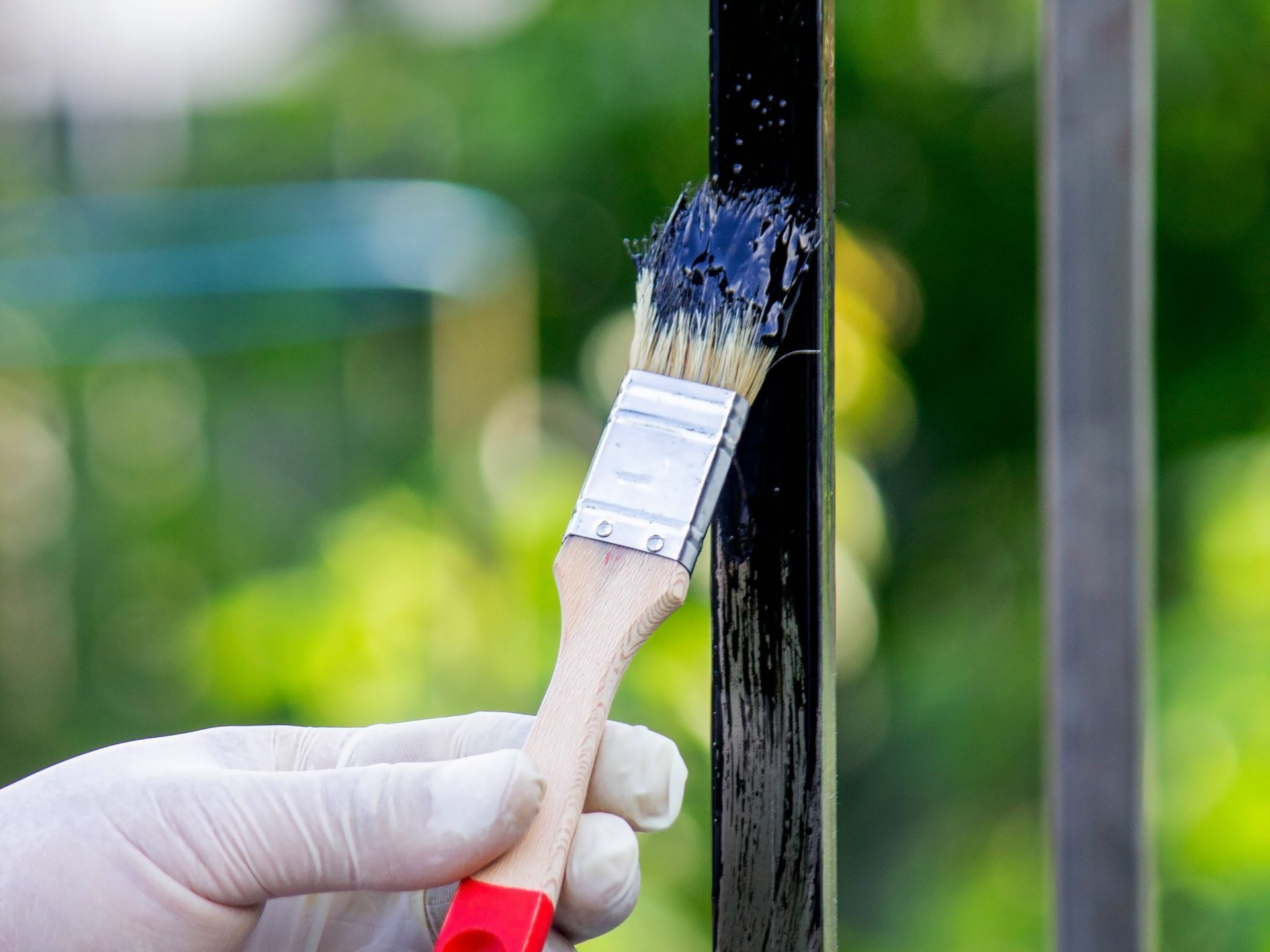 A person is painting a metal fence with a brush.