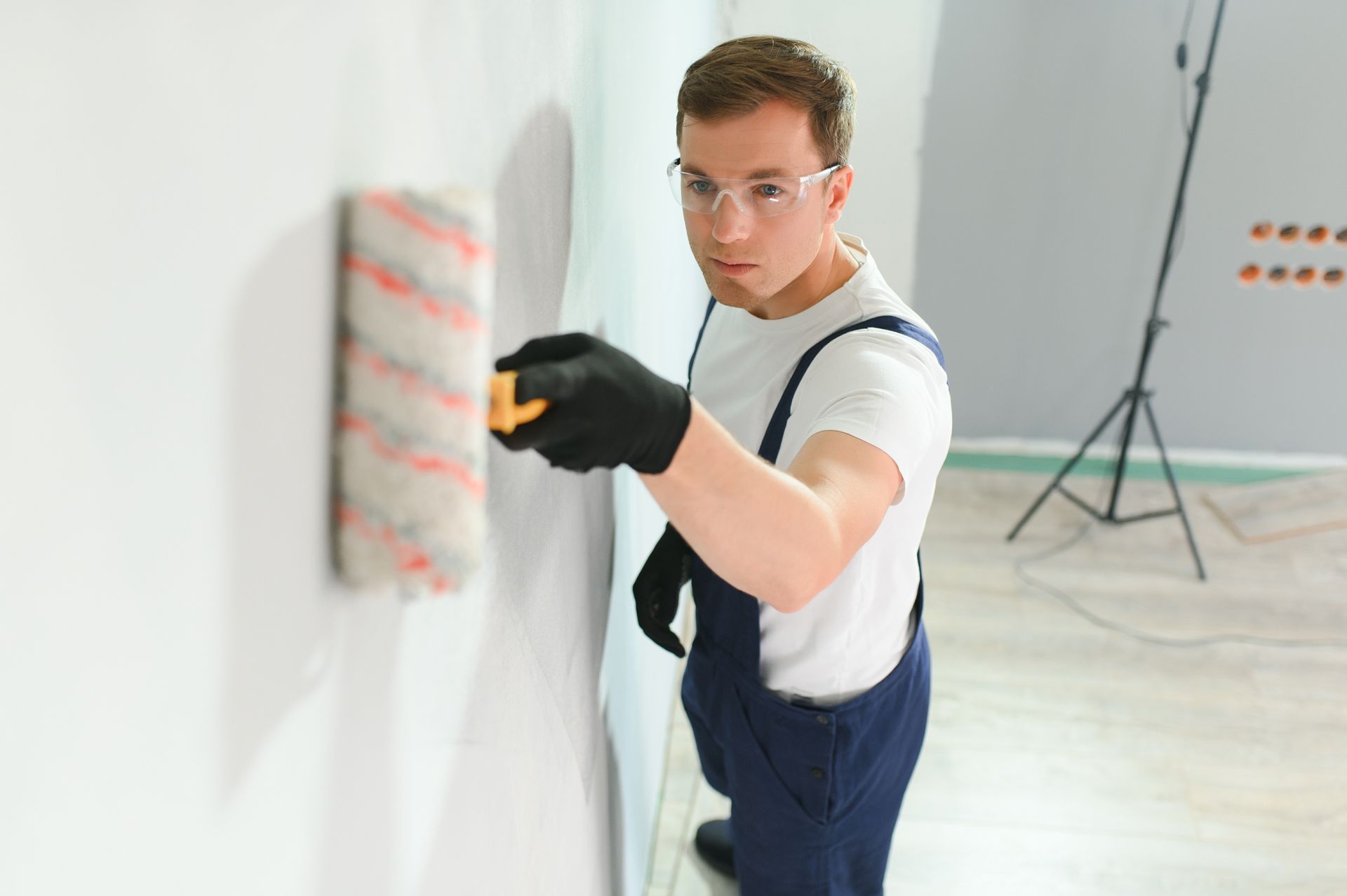 A man is kneeling down while painting a wall with a paint roller.