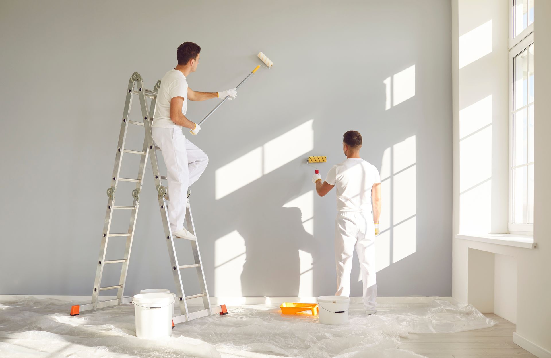 A man is standing on a ladder painting a wall in a room.