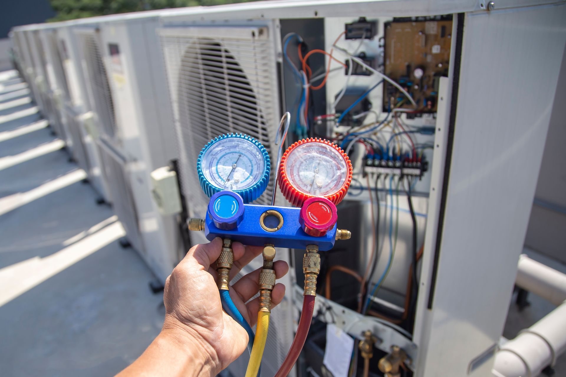 A hand holds an HVAC manifold gauge set while servicing an outdoor air conditioning unit. A hand holds an HVAC manifold gauge set while servicing an outdoor air conditioning unit.