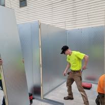 A technician works on an HVAC unit, with a manifold gauge set, tools, and a tool bag nearby on a light-colored floor.