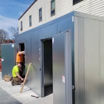 Two technicians in gray uniforms work on installing or repairing a built-in kitchen refrigerator.