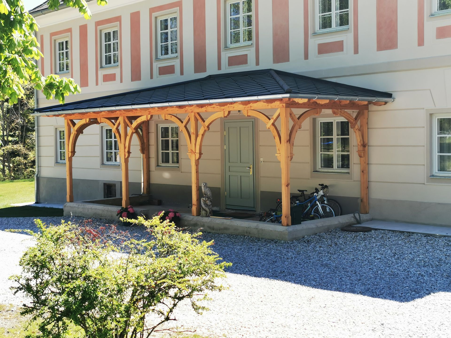 Eine hölzerne Veranda ist an ein rosa-weißes Gebäude angebaut, daneben stehen Fahrräder.