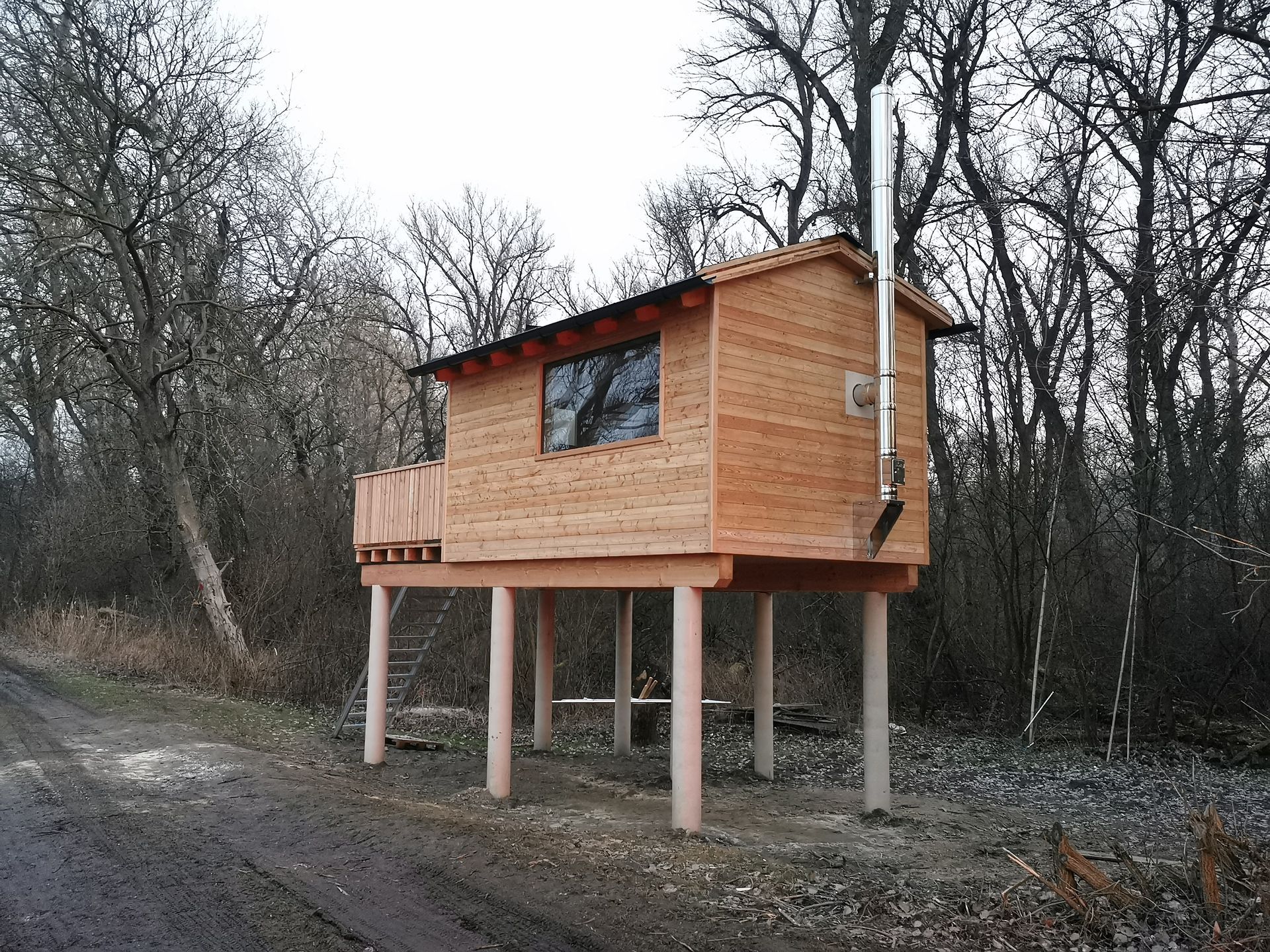 Stelzen gebaute Holzhütte neben einem Feldweg in einem laublosen Wald