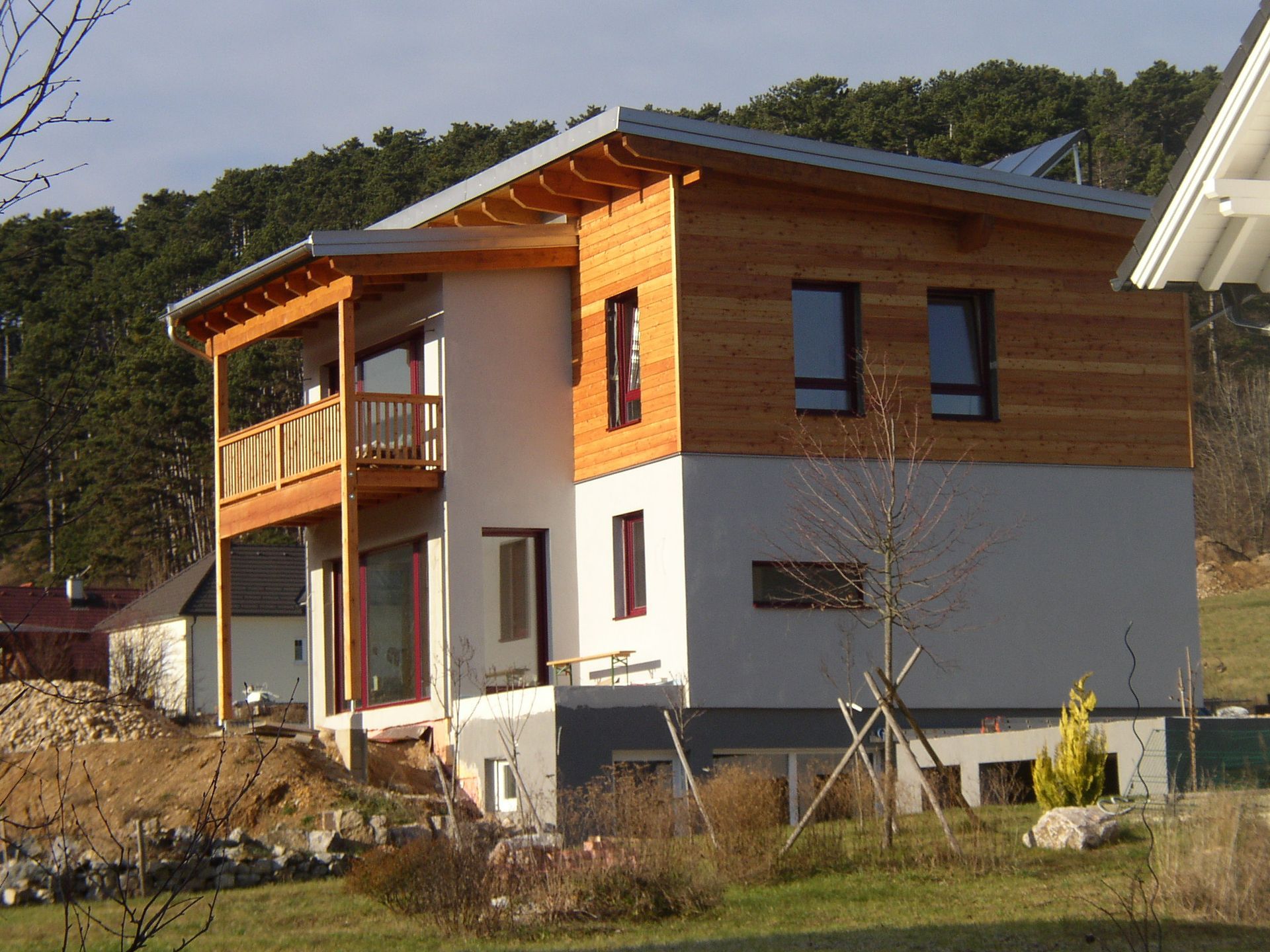 Modernes zweistöckiges Haus mit Holzverkleidung, Balkon und Schrägdach am Hang