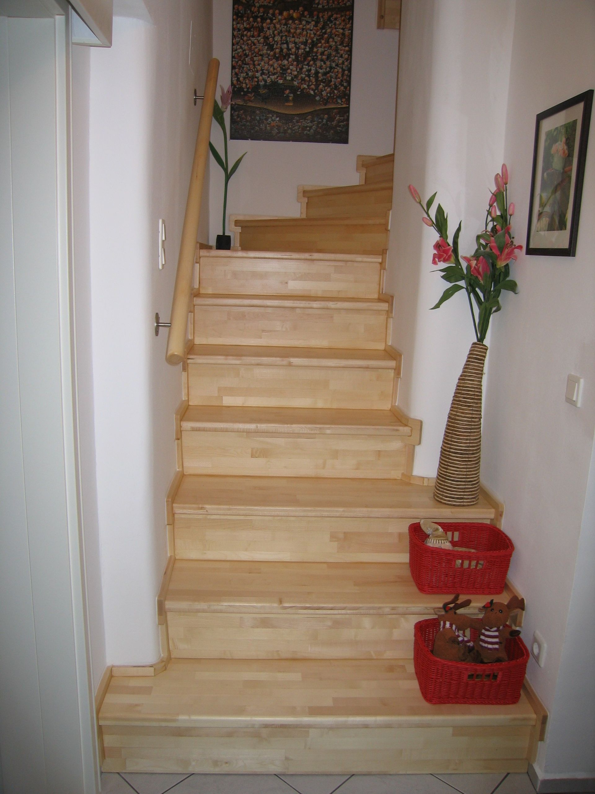 Eine hölzerne Innentreppe mit roten Körben und einer Blumenvase auf dem Treppenabsatz