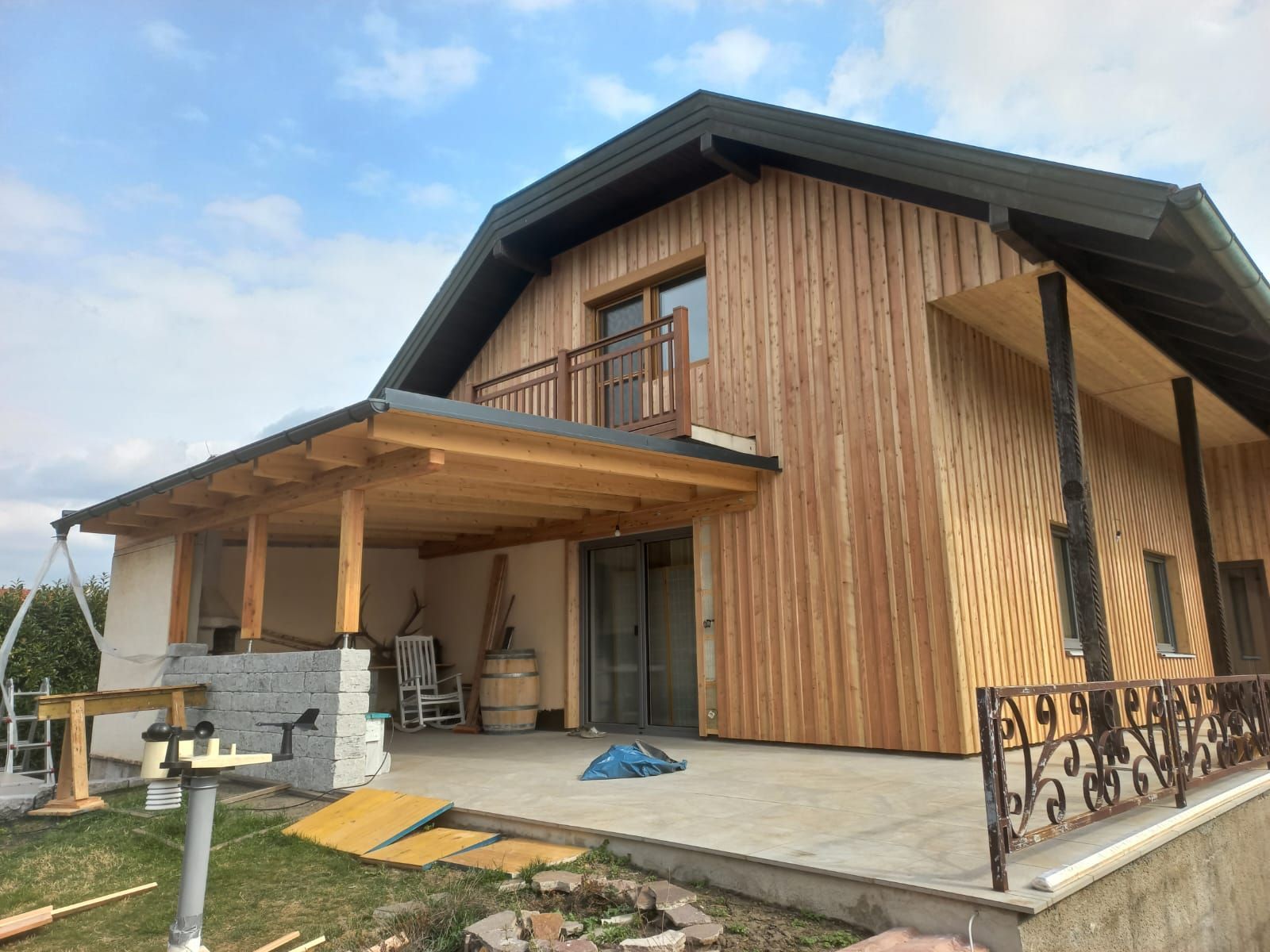 Modernes Holzhaus mit überdachter Veranda, schrägem Dach und großen Fenstern unter einem bewölkten Himmel