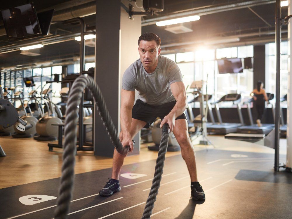 Man exercising with battle ropes in a gym, concentrating.