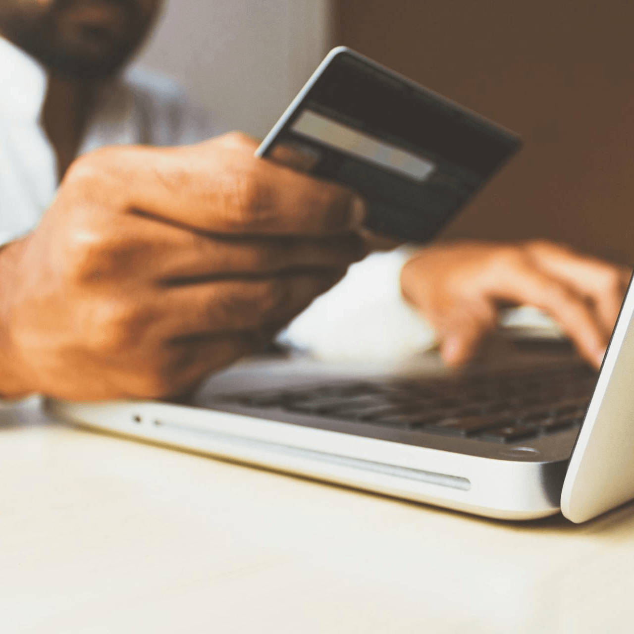 Person holding a credit card while typing on a laptop, presumably online shopping.