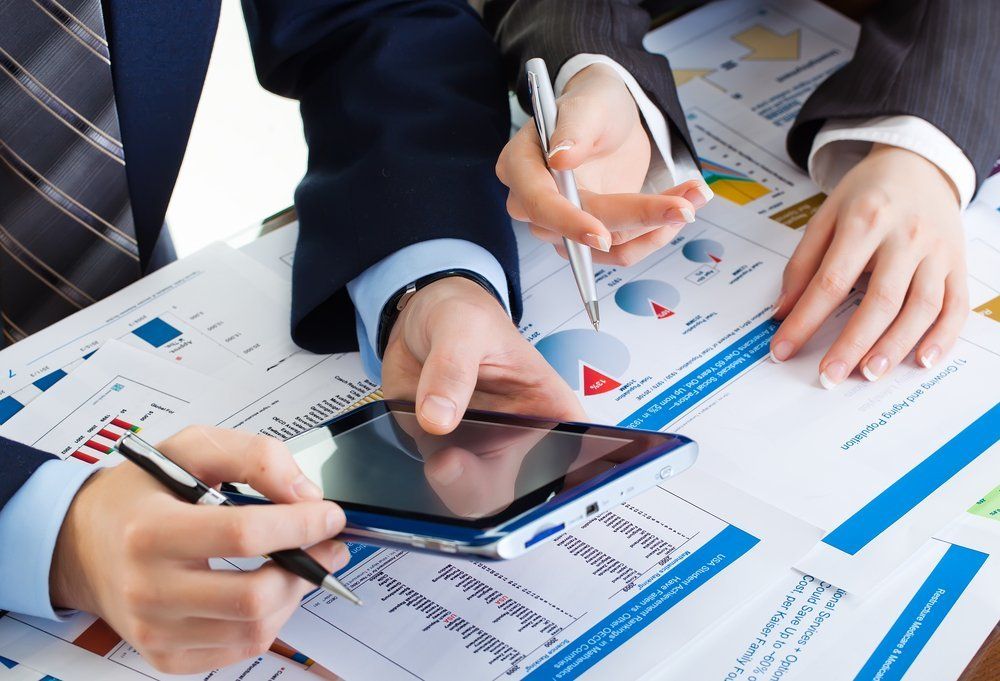 Two people in business attire reviewing financial reports and tablet.