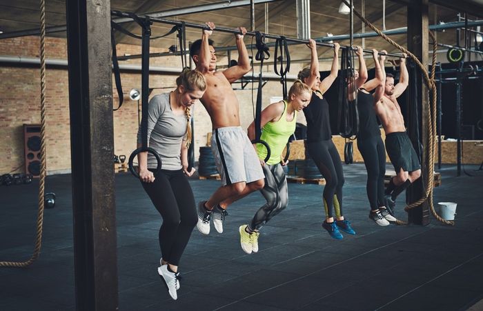 People exercising on gymnastic rings in a gym. They are hanging and looking down.