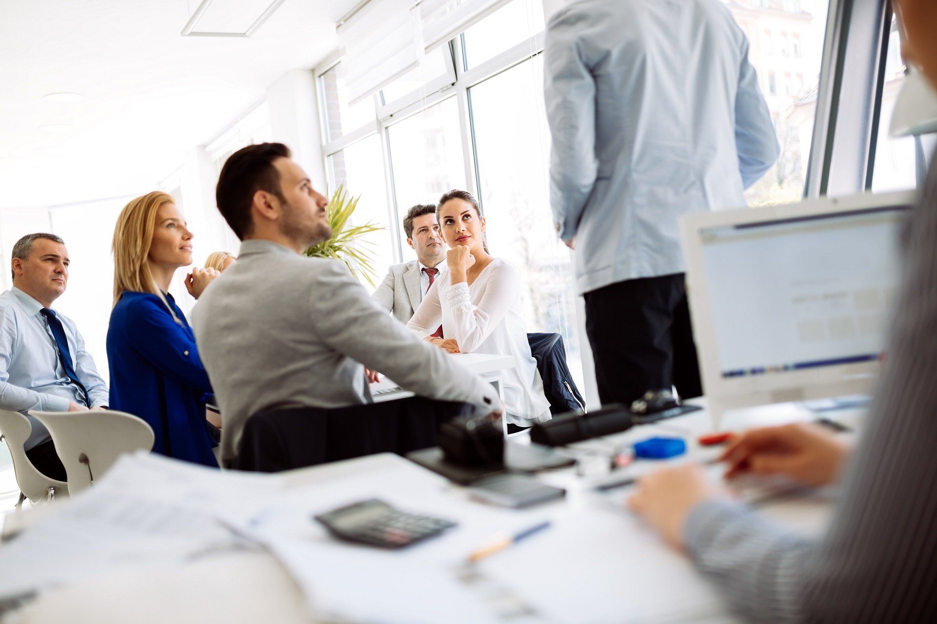 Business meeting in a modern office, people listening attentively as one stands and addresses the group.
