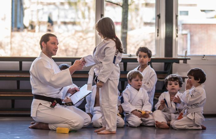 Martial arts instructor shakes hands with a child in a dojo, other children watch.