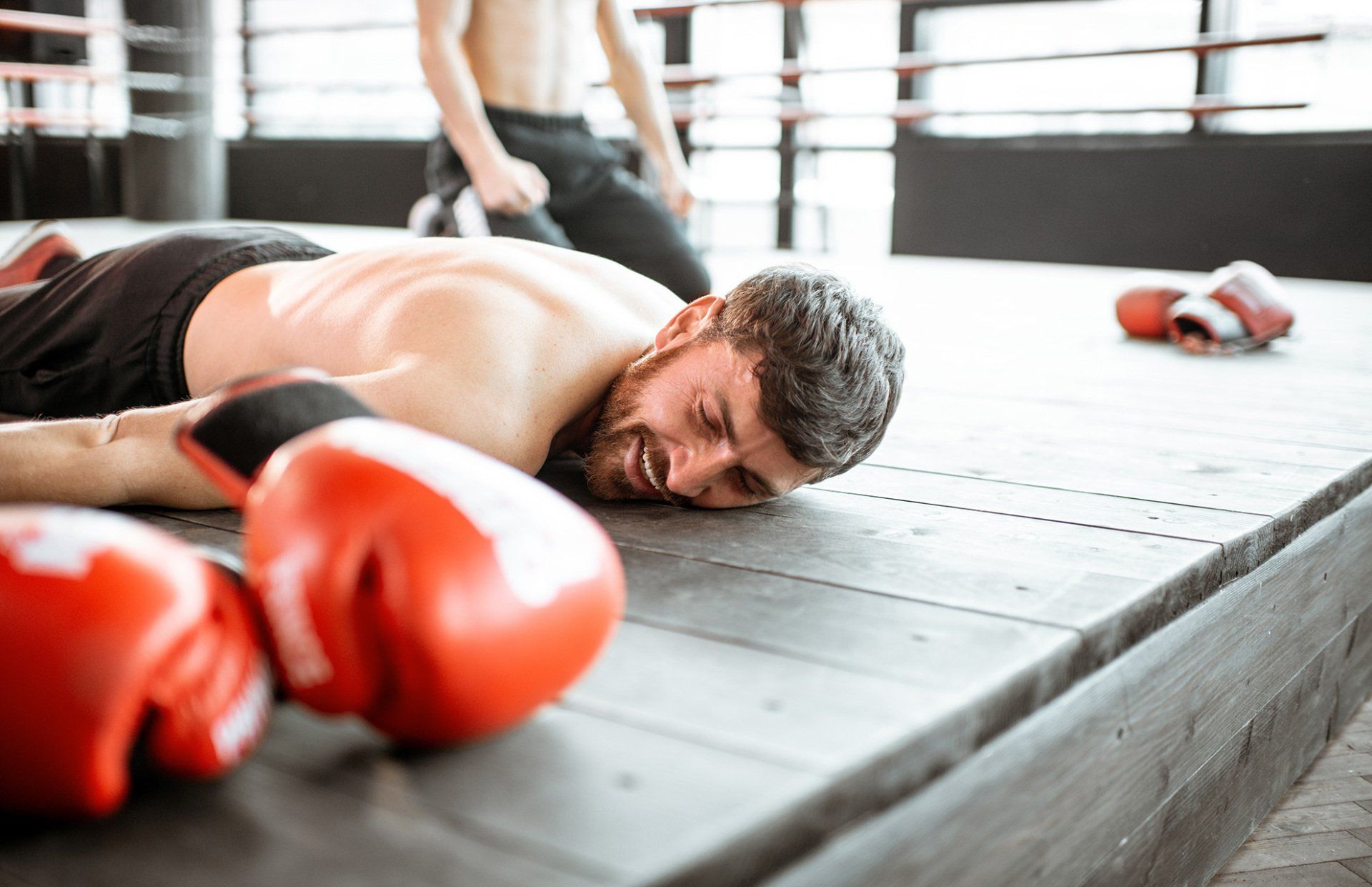 Boxer knocked out on the floor of a boxing ring, red gloves in foreground, another boxer kneeling.