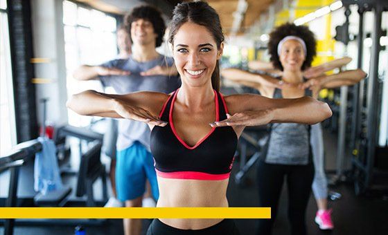 People in a gym stretching their arms out, smiling.