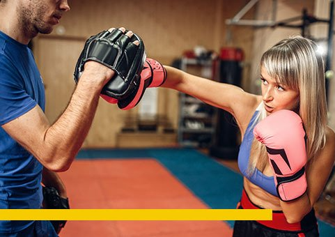 Woman in pink boxing gloves practicing a punch with a trainer in a gym.