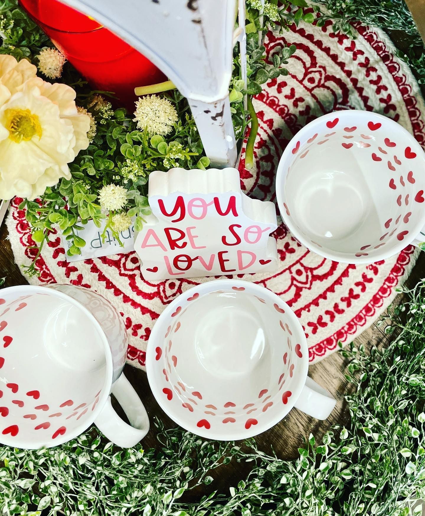 Three mugs with red hearts, nestled on a red and white patterned coaster, with 