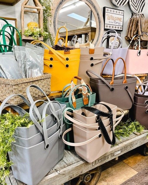 Bags of various colors with leather handles on a wooden cart in a store.