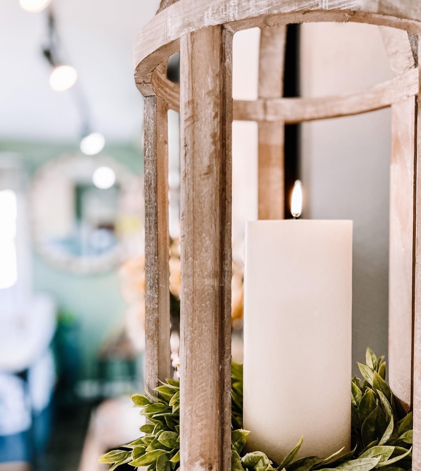 Wooden lantern with lit candle and greenery, in a shop setting.