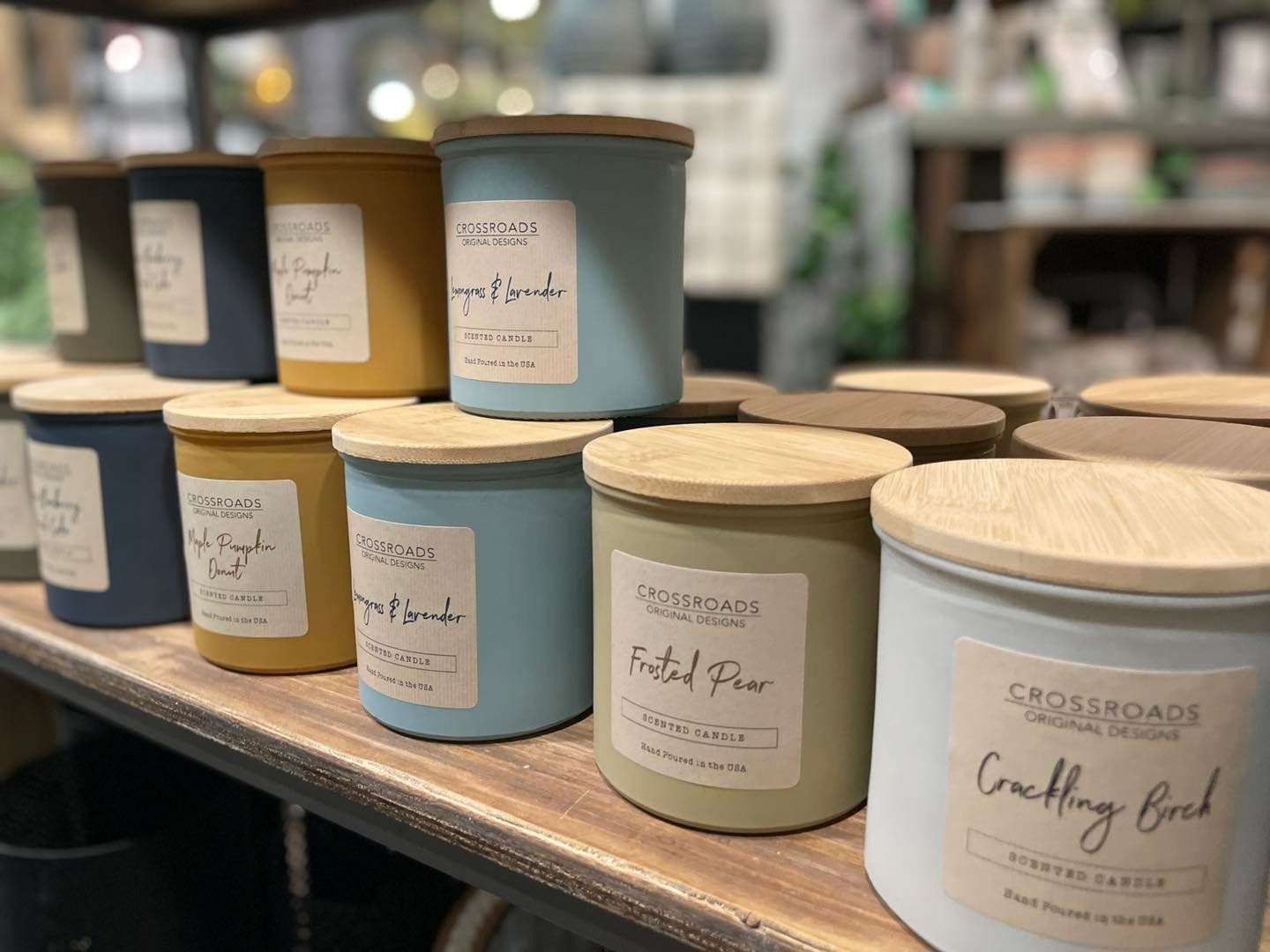 Candles in various colors on a shelf with wooden lids. Labels on the candles.