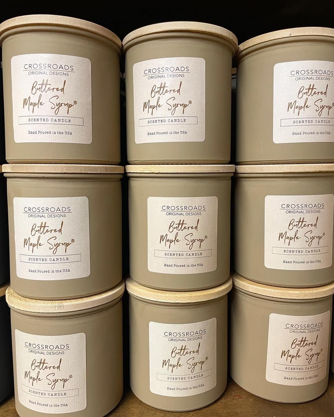 Nine beige candles with labels stacked on a shelf.