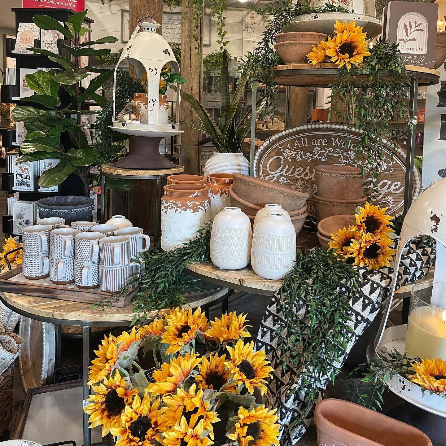 A store display with sunflowers, decorative jars, mugs, and greenery.