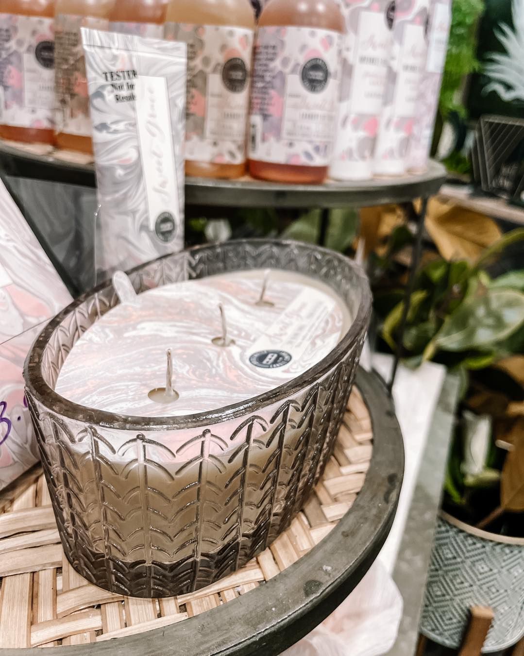 Oval candle with three wicks in patterned glass, sitting on a round woven surface.