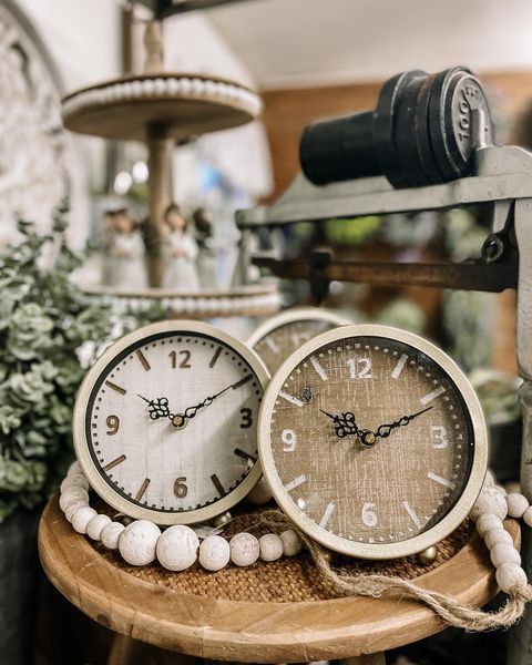 Two beige wooden clocks on a small stool, with decorative beads and other items in the background.
