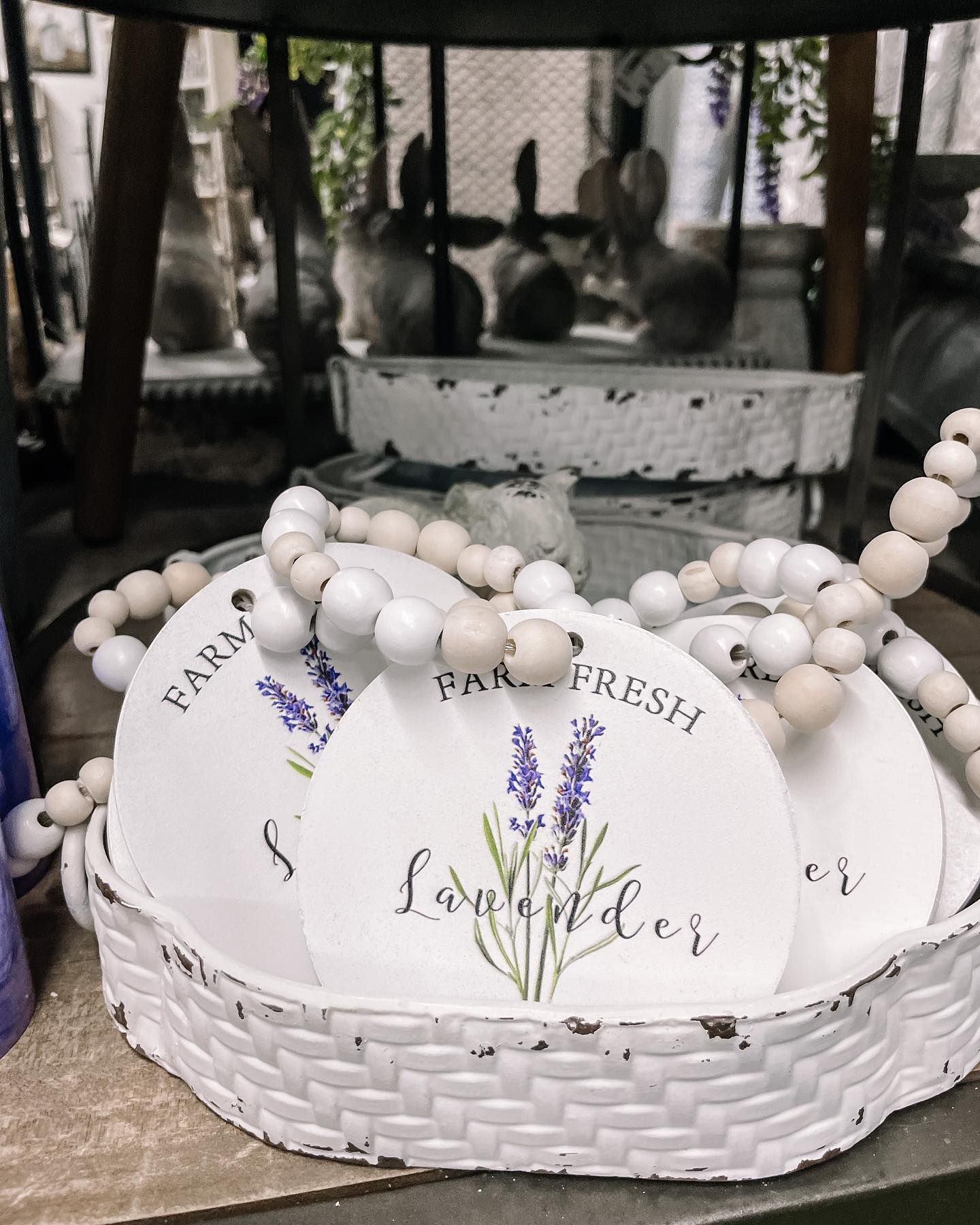 White beaded garland on a white basket holding lavender-themed tags. Background blurred.