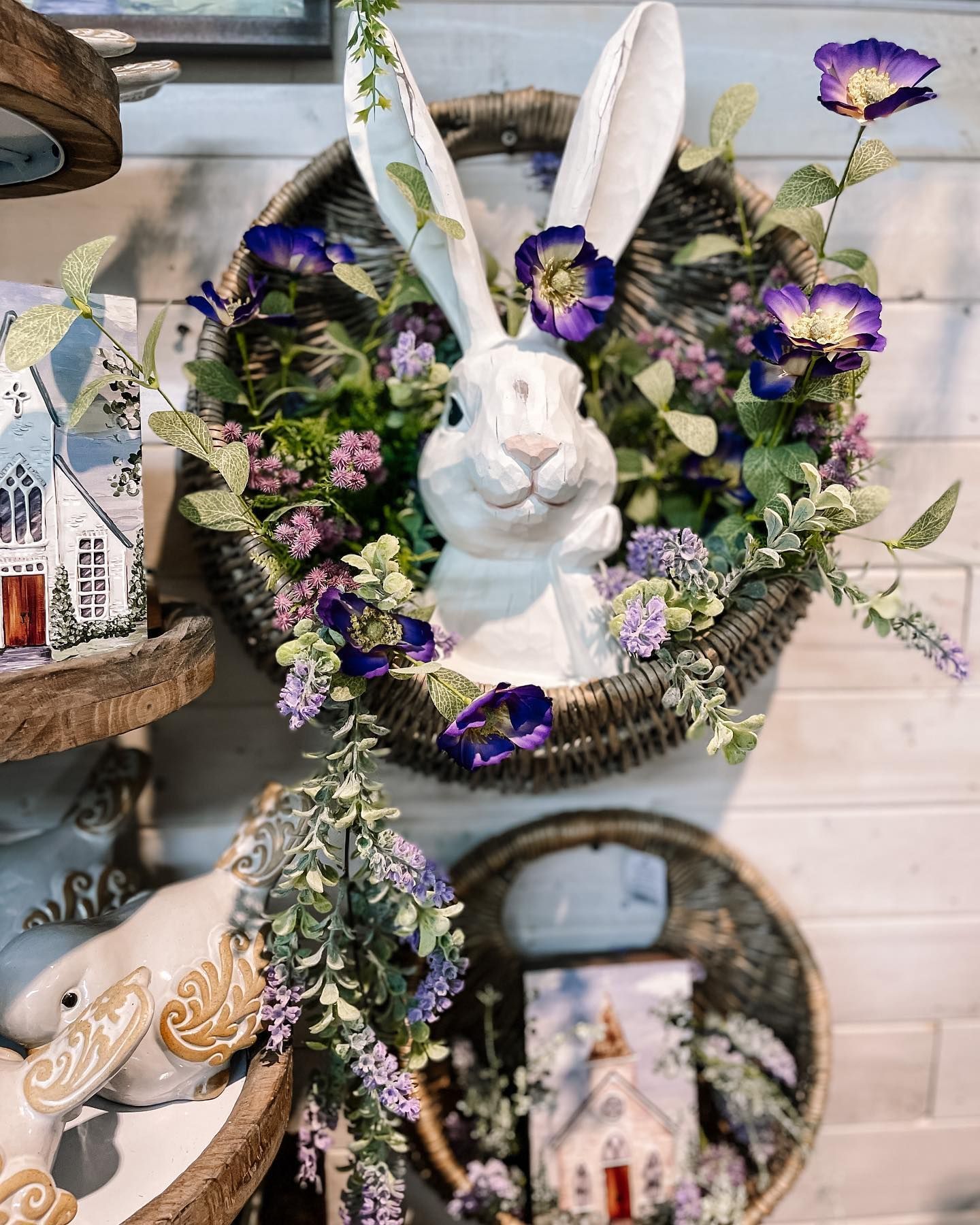 White rabbit head in a floral wreath. Easter decorations on display with buildings.