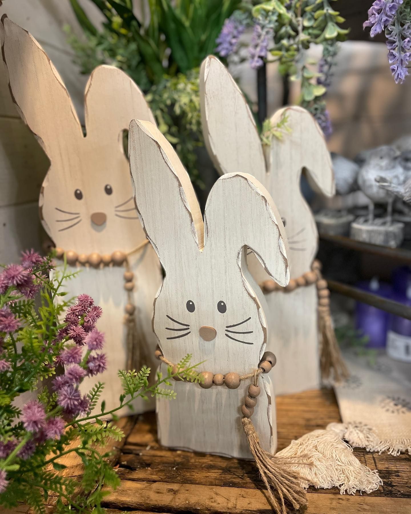 Wooden bunny decorations with beaded accents and tassel, arranged with flowers.